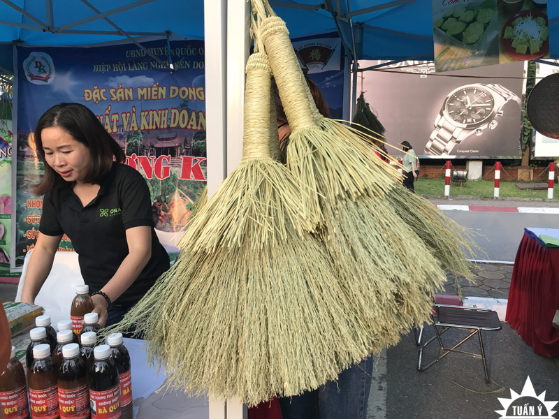 Hình ảnh chiếc chổi lúa thân thuộc treo bán tại hội chợ qua thanh giằng nhà bạt